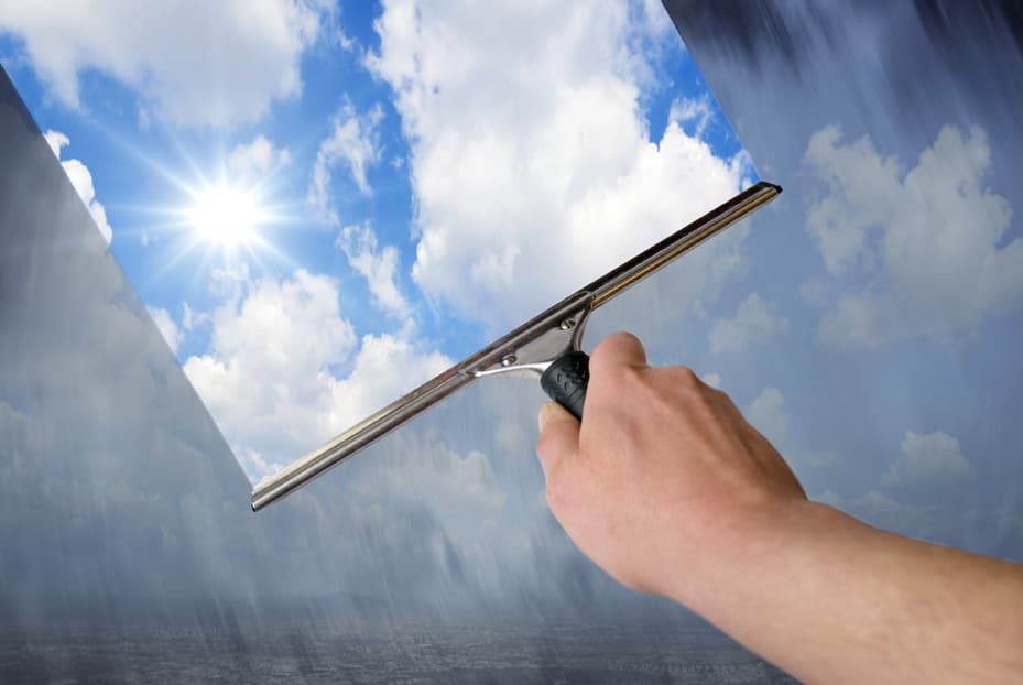 Hand hält Fensterabzieher, durch das Fenster kann man einen blauen Himmel mit Wolken und Sonnenschein sehen | Motiv © Gunnar Assmy - Fotolia.com | © Fotolia.com, März 2014