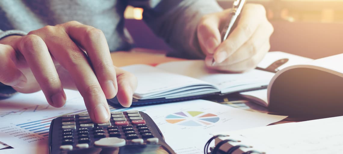 Ausschnitt einer Person am Schreibtisch, die auf einem Taschenrechner tippt und ein Heft vor sich hat | Motiv ©wutzkoh - stock.adobe.com | © stock.adobe.com, November 2020